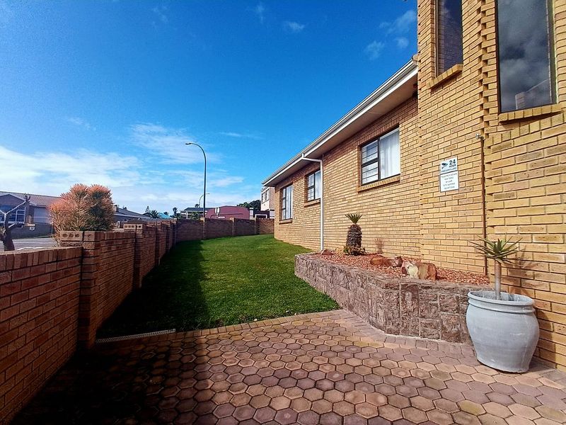 A well-maintained rear exterior featuring a face brick facade, paved patio area, and a neat lawn enclosed by a brick boundary wall.