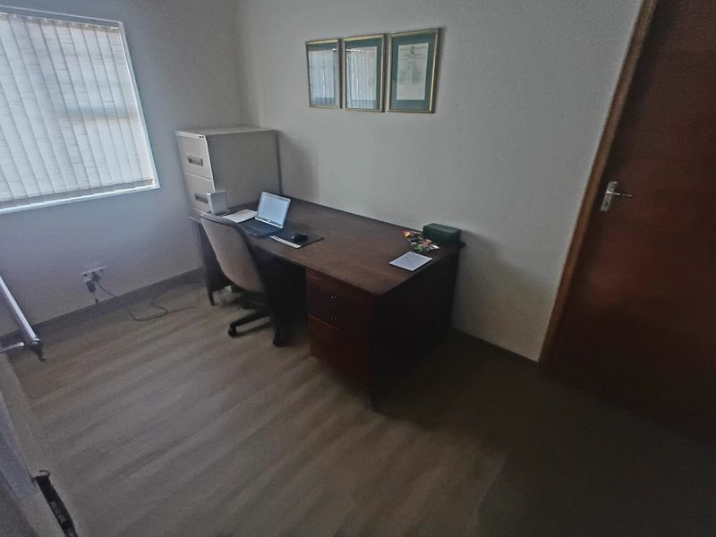 A functional home office space featuring laminate flooring, a window with venetian blinds, and a solid timber door.