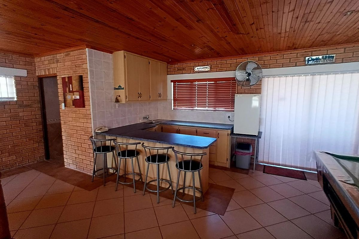 A functional kitchen area featuring exposed brick walls, timber ceiling, tiled flooring, and built-in cabinetry with a breakfast bar counter.