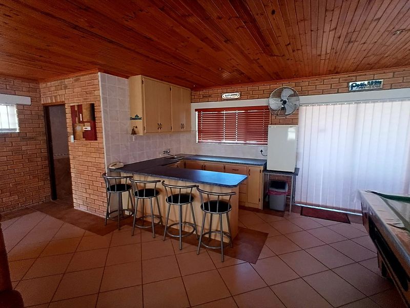 A functional kitchen area featuring exposed brick walls, timber ceiling, tiled flooring, and built-in cabinetry with a breakfast bar counter.