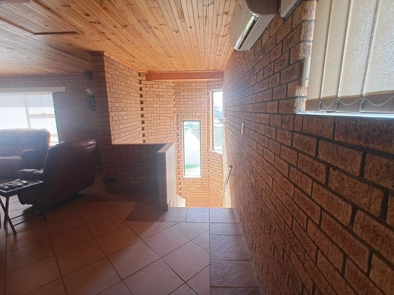 A hallway area featuring exposed brick walls, timber ceiling paneling, and tiled flooring, leading to a staircase with natural light from vertical windows.