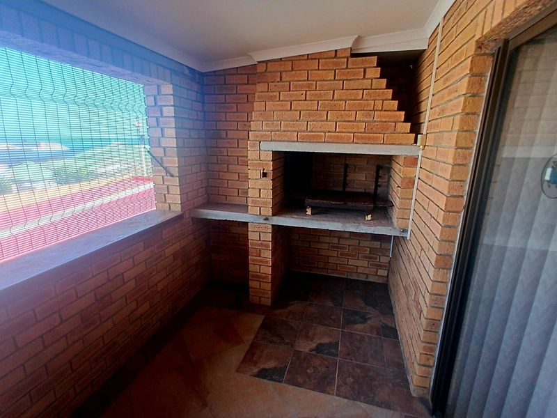 Covered balcony featuring a built-in brick braai, tiled flooring, and exposed brick walls, offering a functional outdoor entertainment space.