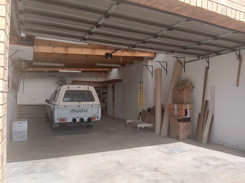 A spacious double garage featuring exposed timber ceiling beams, concrete flooring, and built-in storage shelving, providing ample space for vehicles and workshop use.