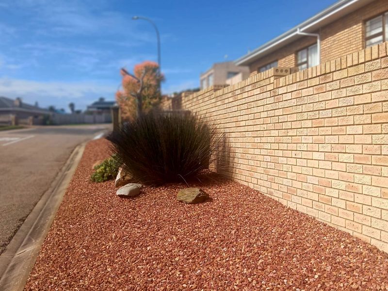 A view of the property's street-facing boundary wall featuring brick construction and low-maintenance gravel landscaping along the roadside.