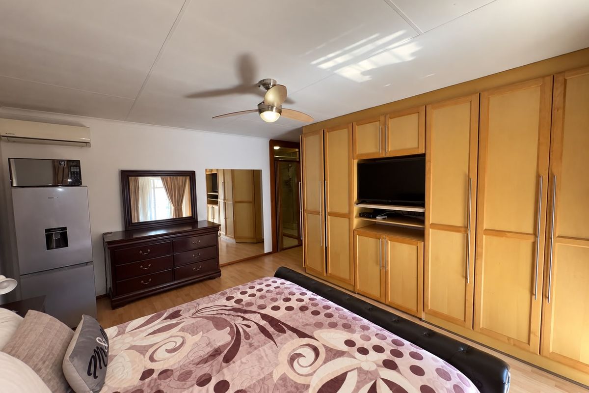 Spacious bedroom featuring extensive built-in wooden cabinetry, laminate flooring, a ceiling fan, and an integrated air conditioning unit.