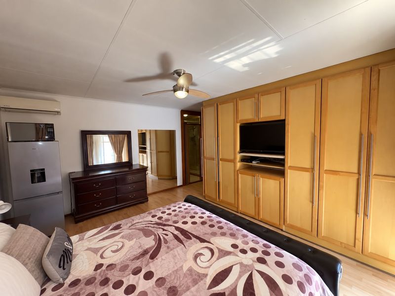 Spacious bedroom featuring extensive built-in wooden cabinetry, laminate flooring, a ceiling fan, and an integrated air conditioning unit.