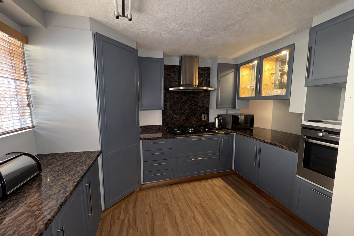 Modern kitchen featuring blue cabinetry, granite countertops, built-in oven, gas hob, stainless steel extractor fan, and glass-fronted display cabinets.