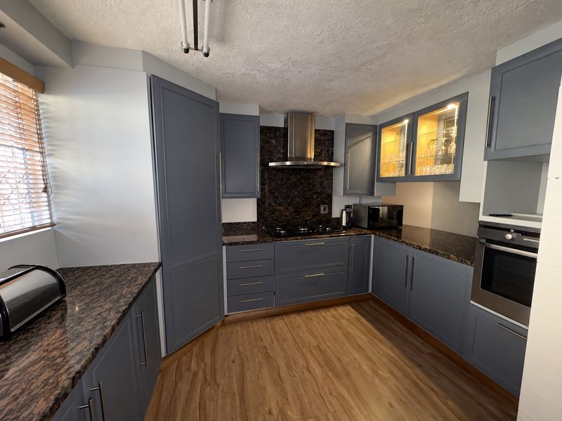 Modern kitchen featuring blue cabinetry, granite countertops, built-in oven, gas hob, stainless steel extractor fan, and glass-fronted display cabinets.