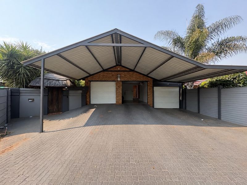 A spacious double garage featuring a large covered carport and a neatly paved driveway, enclosed by a secure perimeter wall.