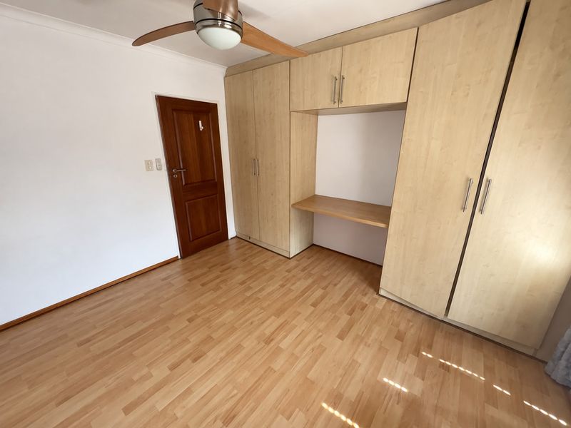 A clean, empty bedroom featuring light wood-look laminate flooring, a ceiling fan, and extensive built-in cabinetry with an integrated desk area.