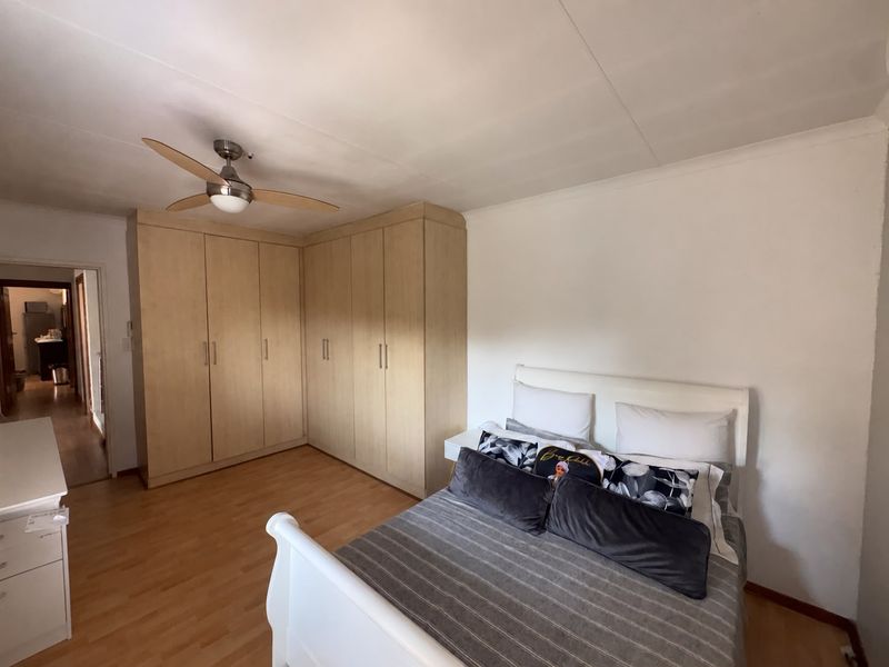 A well-maintained bedroom featuring light wood-toned built-in cupboards, a ceiling fan, and laminate flooring, offering a clean and functional living space.