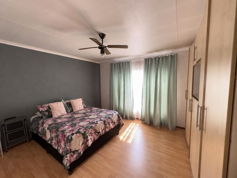 A well-lit bedroom featuring laminate flooring, a ceiling fan, and extensive built-in cupboard storage.