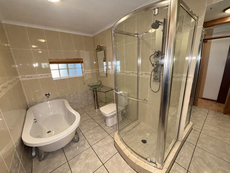 A functional bathroom featuring a freestanding bathtub, a separate glass-enclosed shower, and a glass vessel sink with neutral wall and floor tiling.