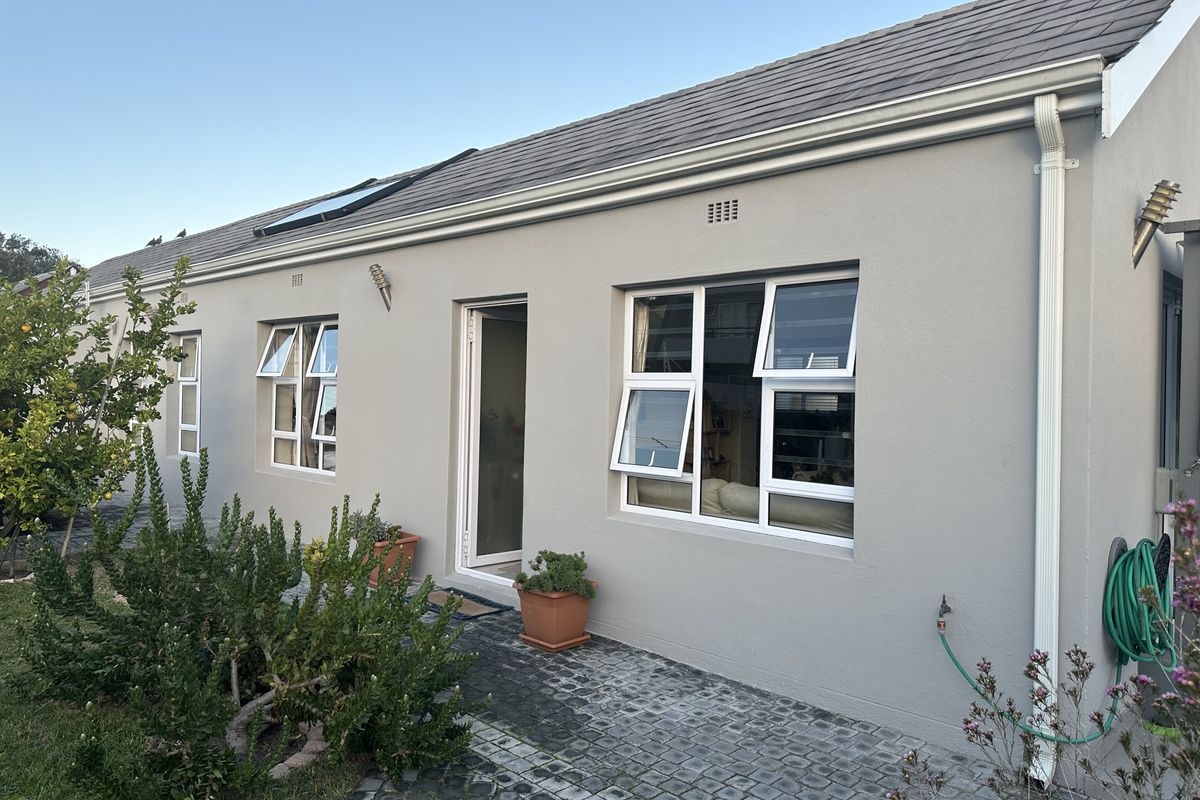Rear exterior view of the house featuring a paved patio, white aluminium windows, tiled roof with a skylight, and well-maintained exterior walls.