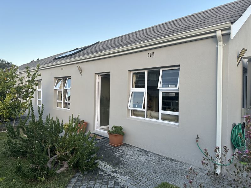 Rear exterior view of the house featuring a paved patio, white aluminium windows, tiled roof with a skylight, and well-maintained exterior walls.
