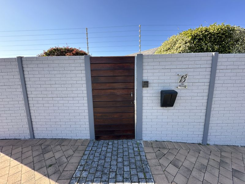 Front entrance featuring a secure timber pedestrian gate, brick boundary wall with electric fencing, and a neat cobblestone walkway leading to the property.