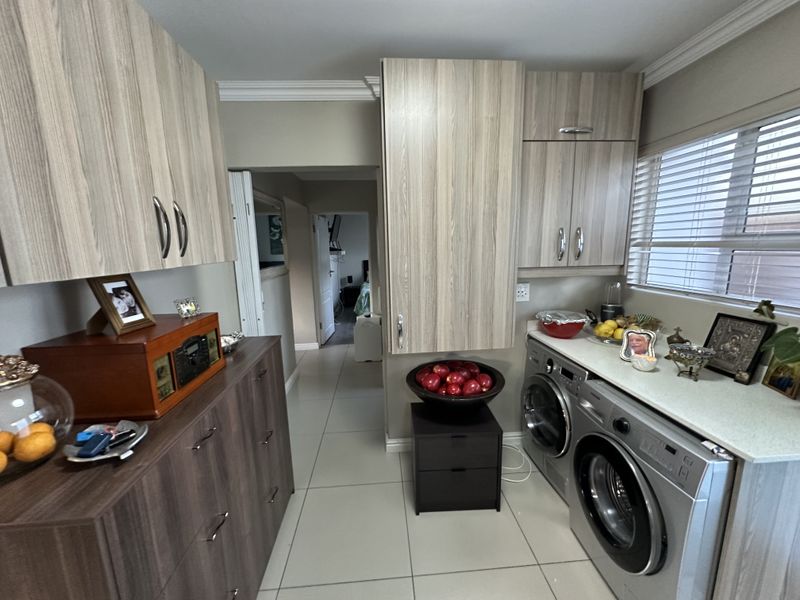 A functional laundry room featuring modern wood-grain cabinetry, stone countertops, tiled flooring, and integrated space for laundry appliances.