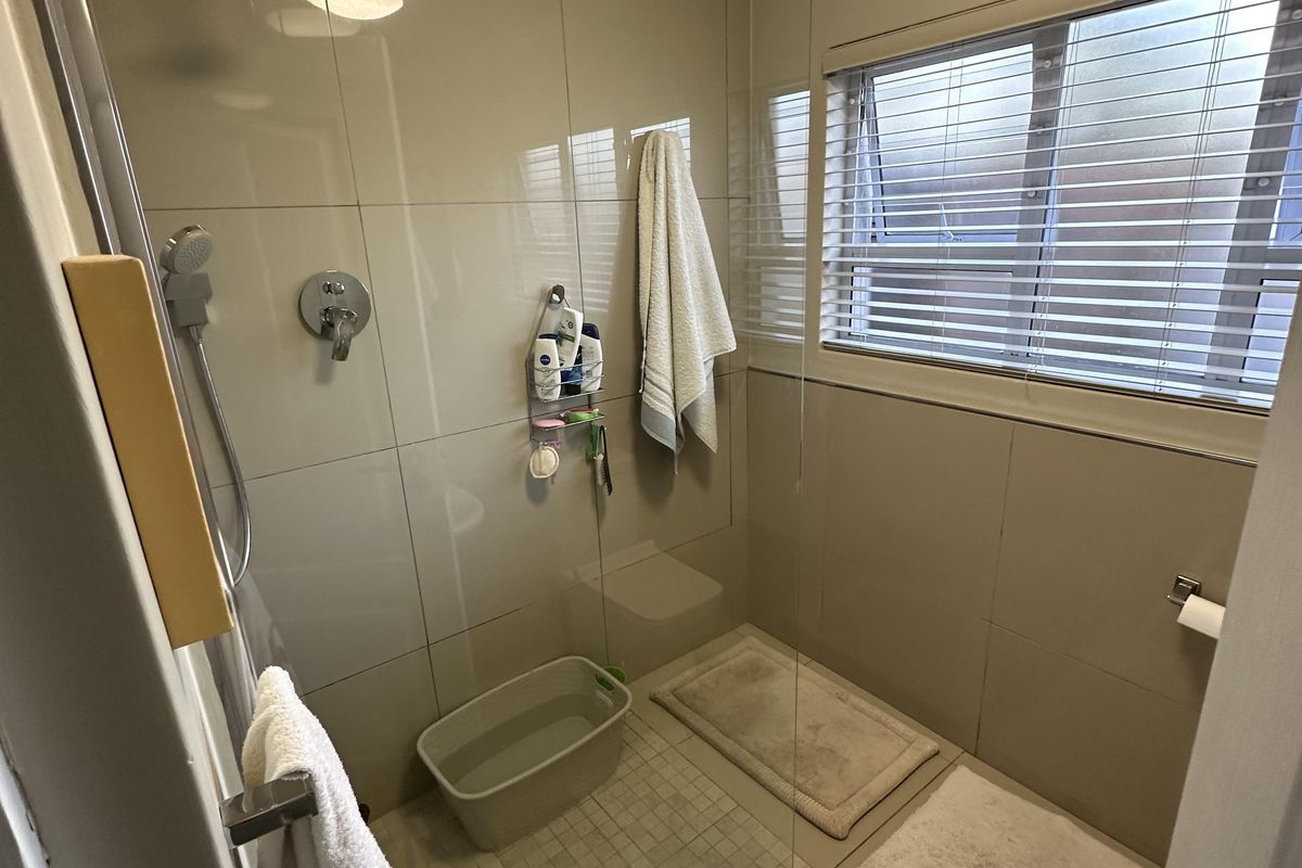 A modern bathroom featuring a walk-in shower with glass screen, neutral wall tiling, and a ceiling extractor fan.