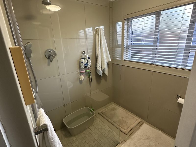 A modern bathroom featuring a walk-in shower with glass screen, neutral wall tiling, and a ceiling extractor fan.