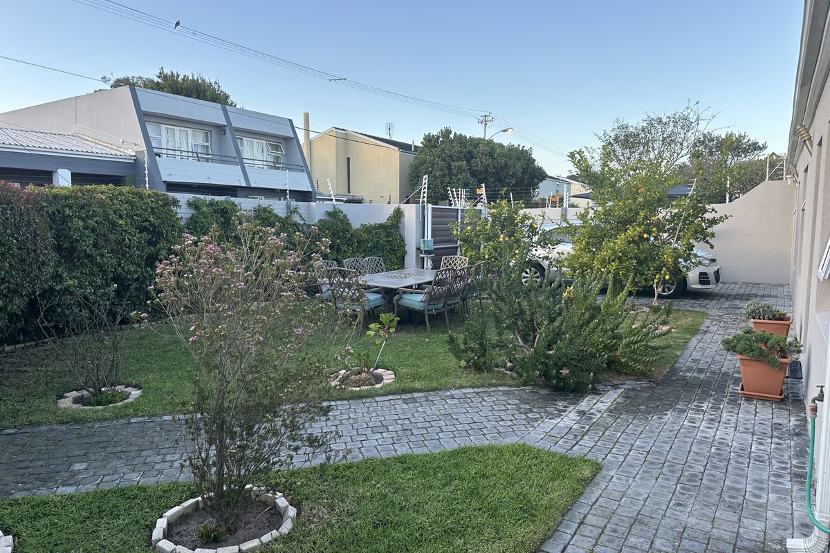 A well-maintained rear garden featuring paved pathways, established greenery, and secure boundary walling with electric fencing.