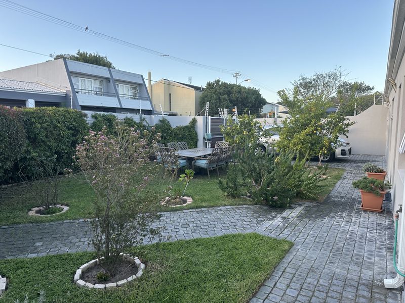 A well-maintained rear garden featuring paved pathways, established greenery, and secure boundary walling with electric fencing.