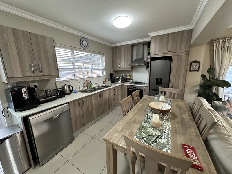 Modern open-plan kitchen featuring wood-look cabinetry, stainless steel appliances, tiled flooring, and a seamless transition to the dining area.