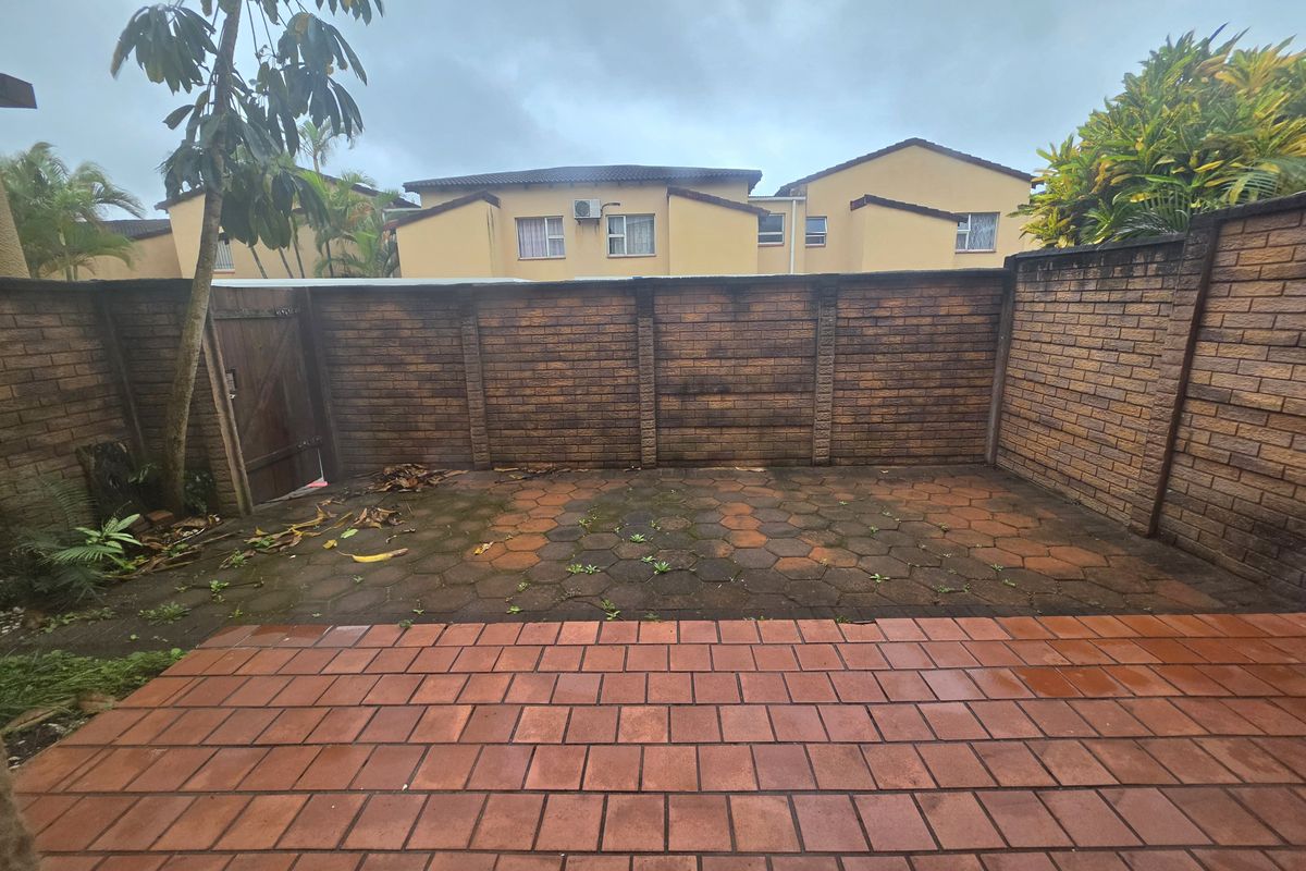 A private rear courtyard featuring a paved patio area enclosed by brick boundary walls and a wooden access gate.