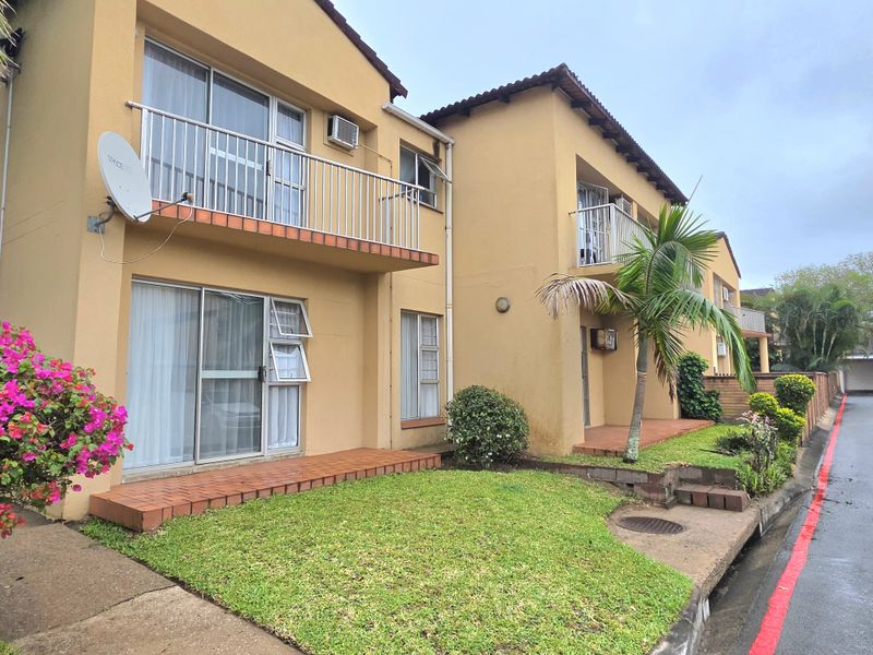 Exterior view of a two-story apartment complex featuring balconies, sliding glass doors, and a small front garden area.
