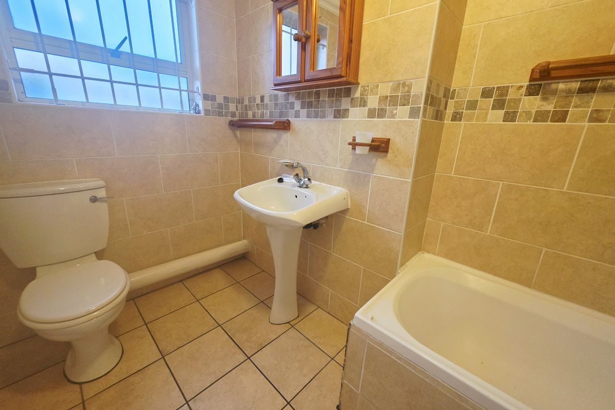 A functional bathroom featuring a pedestal basin, toilet, and bathtub with neutral wall and floor tiling, complemented by a wooden medicine cabinet.