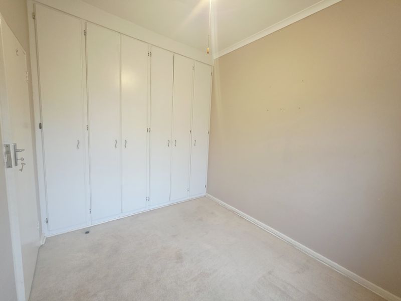 A vacant bedroom featuring neutral walls, carpeted flooring, and extensive built-in storage cupboards.