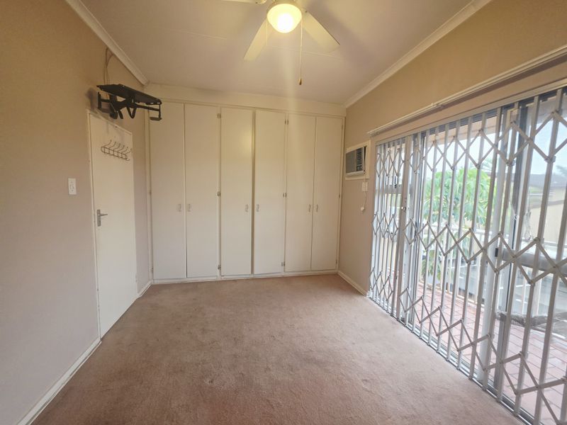 A spacious bedroom featuring built-in cupboards, a ceiling fan, and a sliding glass door with a security gate leading to an outdoor area.