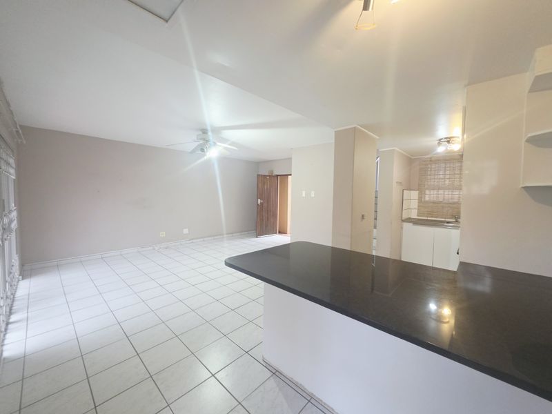 Spacious open-plan living and kitchen area featuring tiled flooring, a granite breakfast counter, and neutral wall finishes in a vacant apartment setting.