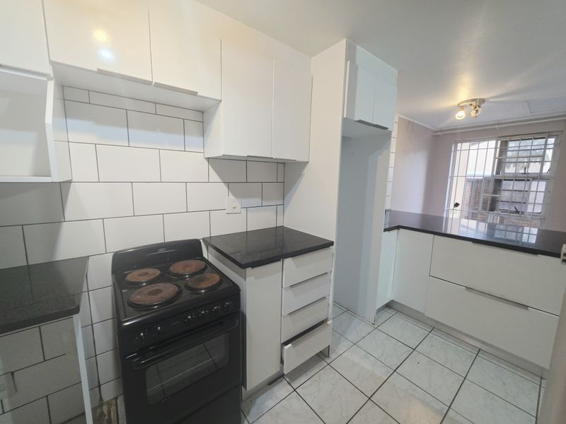 A functional kitchen featuring white cabinetry, black granite countertops, subway tile backsplash, and a freestanding electric stove with tiled flooring.
