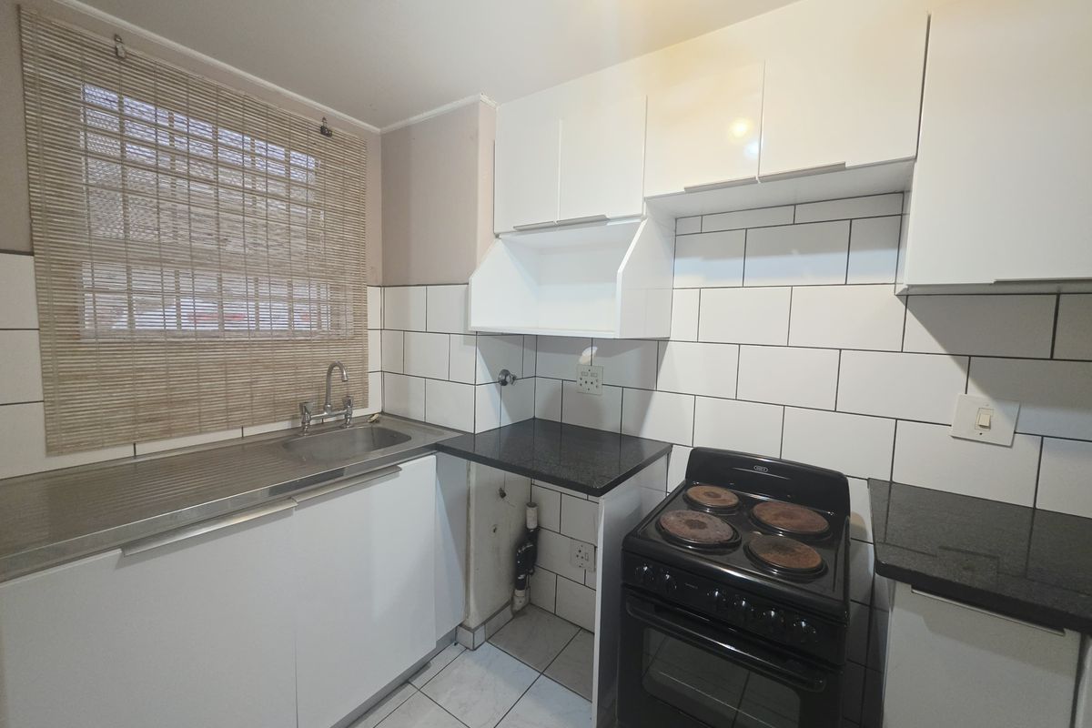 Compact kitchen featuring white cabinetry, black granite countertops, subway tile backsplash, and a freestanding electric stove.
