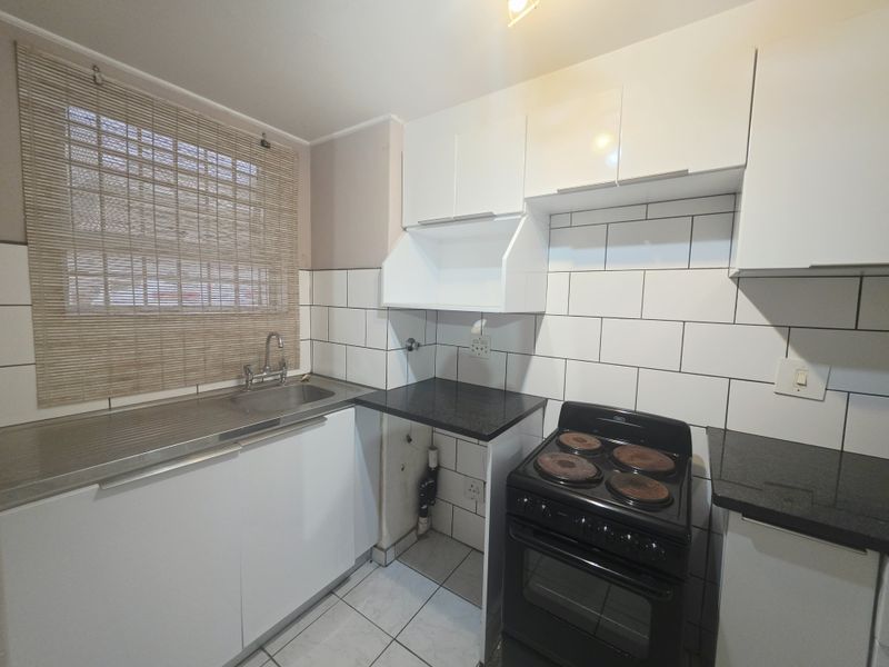 Compact kitchen featuring white cabinetry, black granite countertops, subway tile backsplash, and a freestanding electric stove.