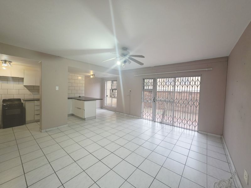 An open-plan living and kitchen area featuring tiled flooring, a ceiling fan, and direct access to an outdoor space through a security-gated sliding door.