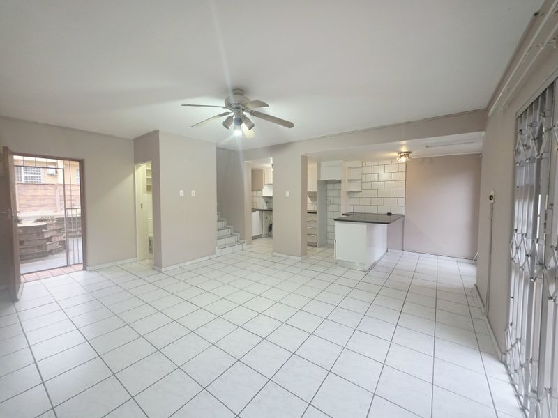 Spacious open-plan living and kitchen area featuring tiled flooring, a breakfast bar, and direct access to an outdoor patio through a security gate.