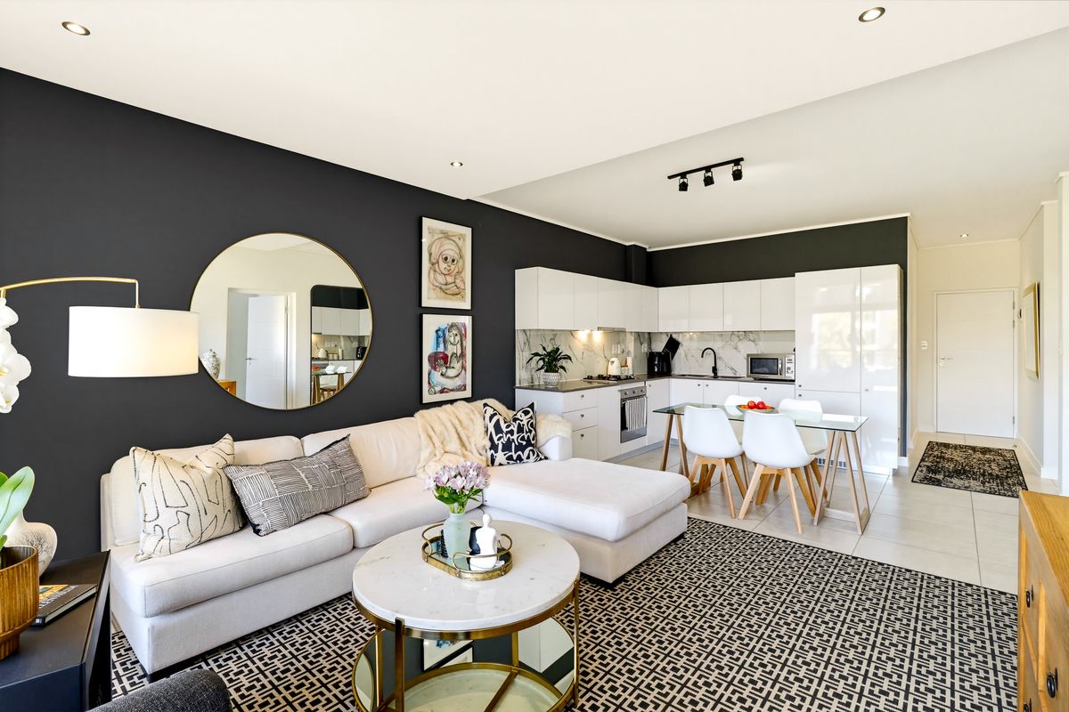Modern open-plan living area featuring a sleek kitchen with white cabinetry, integrated appliances, and tiled flooring, seamlessly flowing into the lounge space.