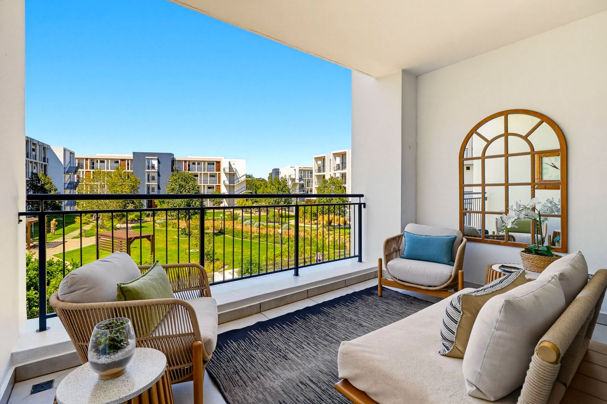 A spacious covered balcony featuring a metal balustrade and tiled flooring, overlooking a well-maintained communal garden area.