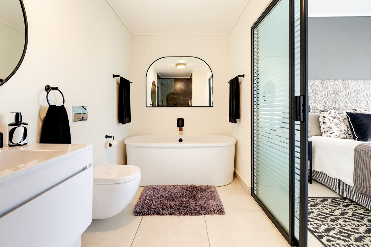 Modern en-suite bathroom featuring a sleek freestanding bathtub, wall-hung toilet, and contemporary vanity, seamlessly connected to the bedroom via a sliding glass door.