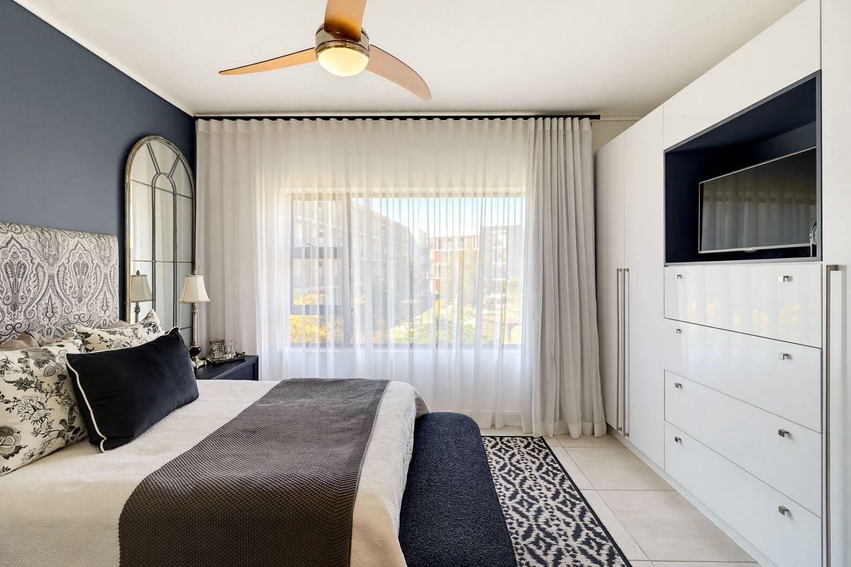 A well-maintained bedroom featuring built-in cupboards, tiled flooring, and a ceiling fan, offering a clean and modern living space.