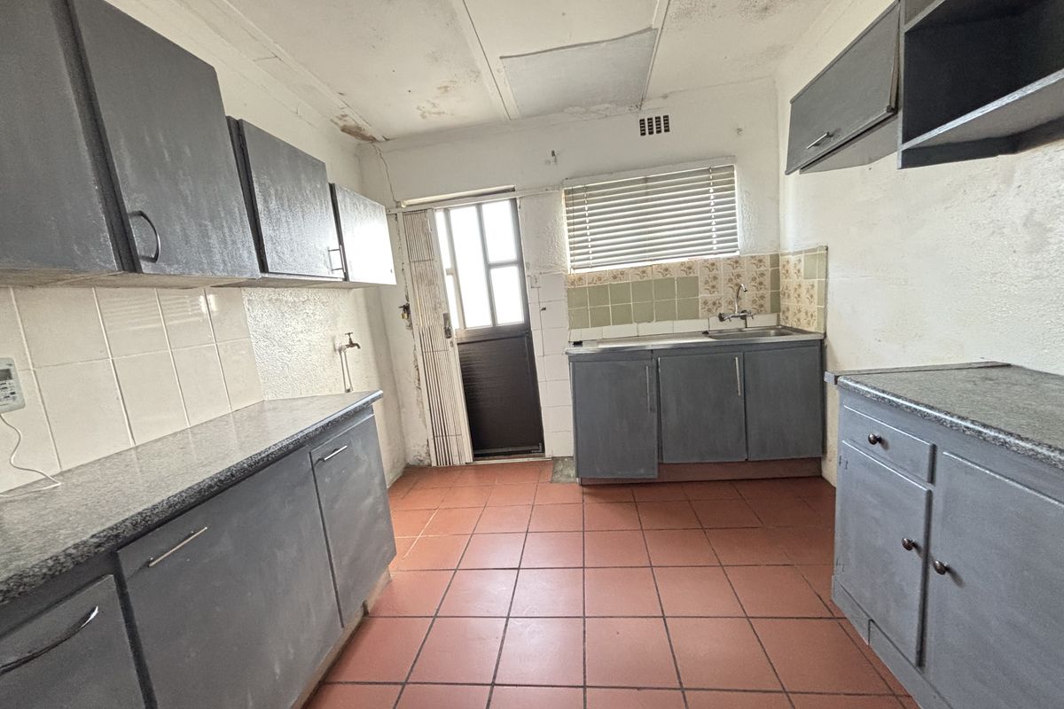 A dated kitchen featuring built-in cabinetry, stone countertops, and tiled flooring, requiring renovation to address ceiling and wall surface deterioration.
