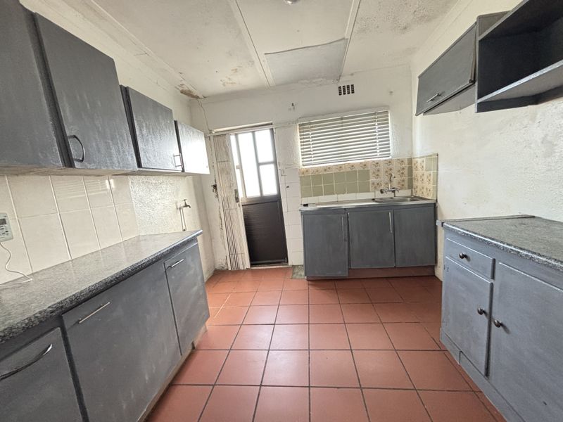 A dated kitchen featuring built-in cabinetry, stone countertops, and tiled flooring, requiring renovation to address ceiling and wall surface deterioration.