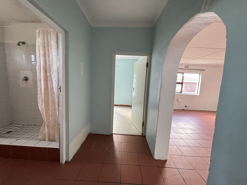A functional hallway area featuring tiled flooring, an arched entryway, and direct access to a shower room and adjacent living space.