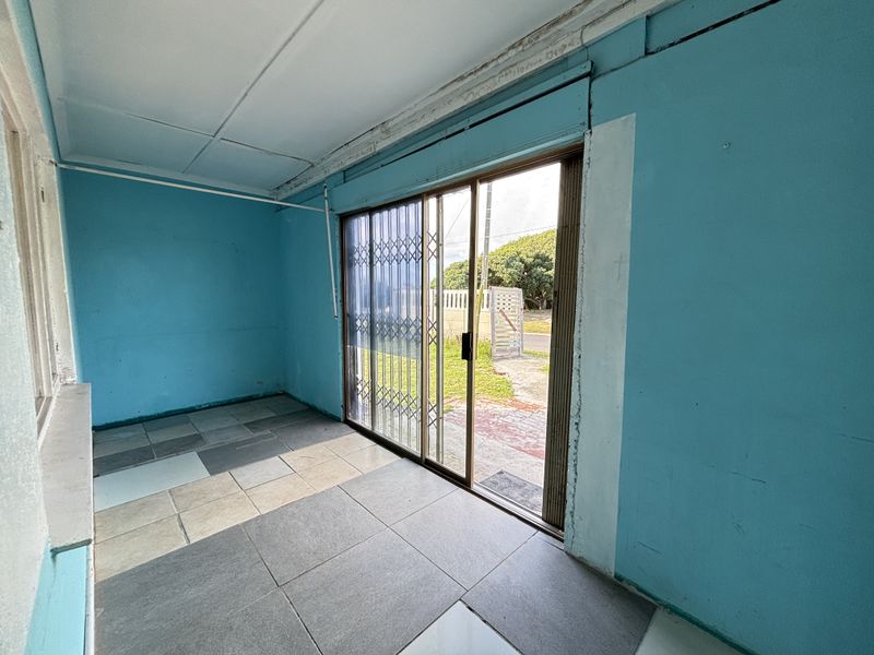 An empty, enclosed patio area featuring sliding glass doors with security gates and mismatched floor tiling, requiring cosmetic updates and repairs.