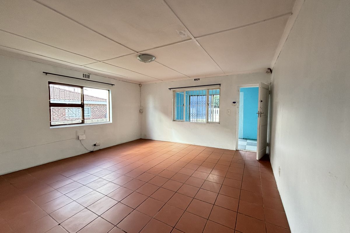 An empty living room featuring terracotta-style floor tiles, security bars on windows, and a simple ceiling finish, offering a blank canvas for renovation.