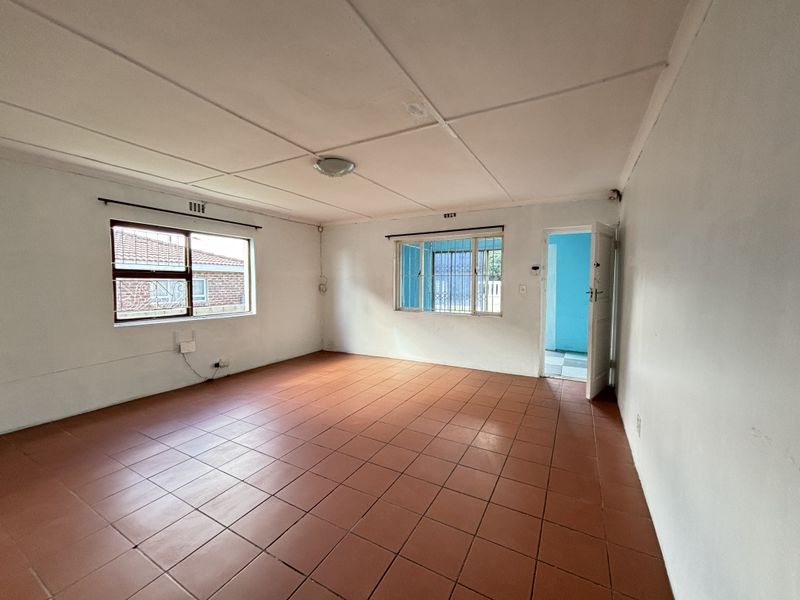 An empty living room featuring terracotta-style floor tiles, security bars on windows, and a simple ceiling finish, offering a blank canvas for renovation.