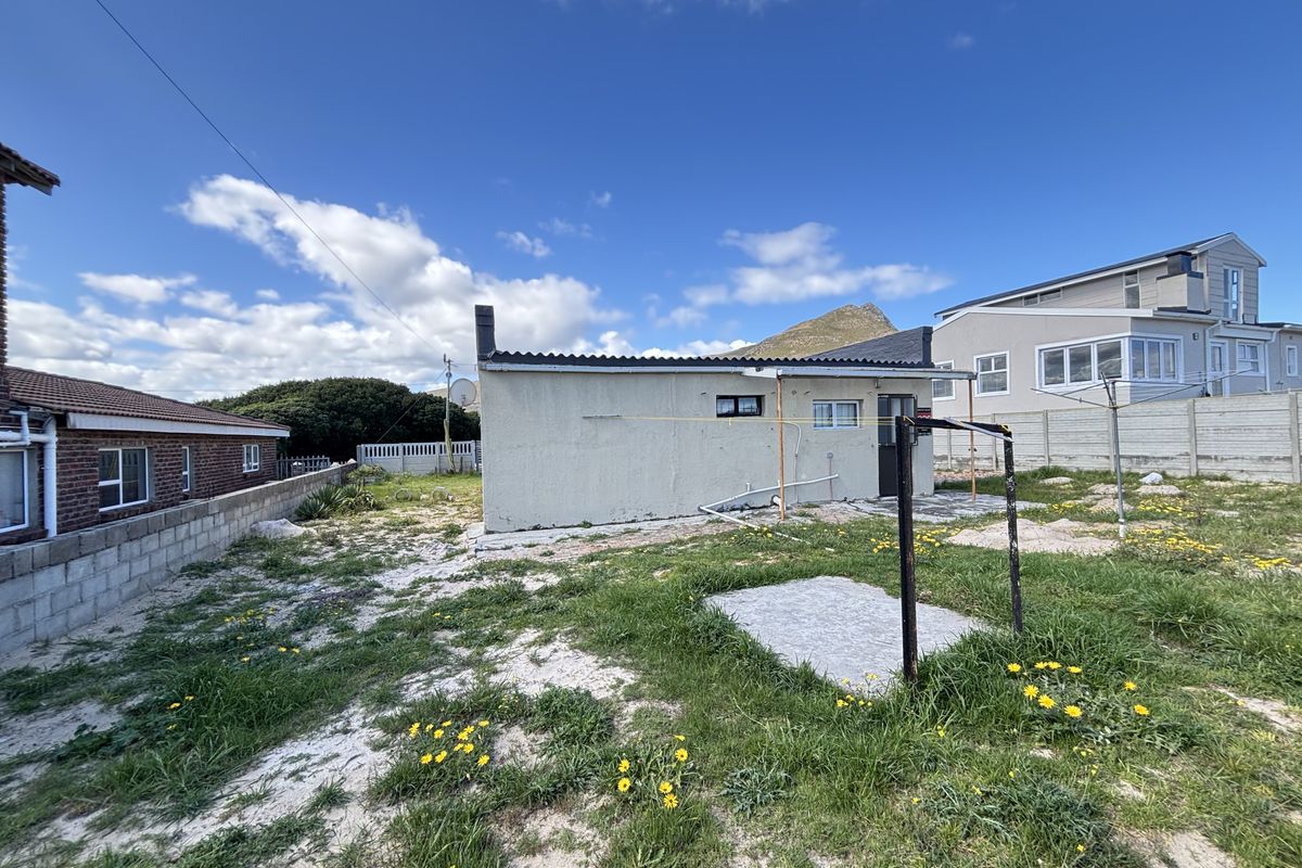 Rear view of the property showing a detached structure, concrete boundary walls, and an unlandscaped garden area.