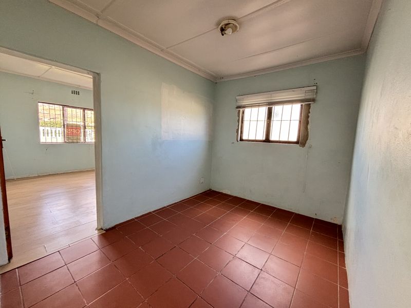 An empty bedroom featuring tiled flooring and security bars on the windows, requiring cosmetic updates to the wall finishes.