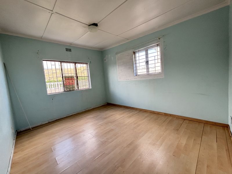 An empty bedroom featuring laminate flooring, security bars on the windows, and a ceiling light fixture, requiring cosmetic updates to the wall finishes.